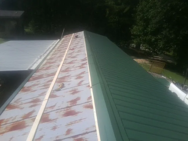 Old rusted panels beside newly installed green metal roofing — Wind Damage Roof Repair by Roofing Brothers in Douglas