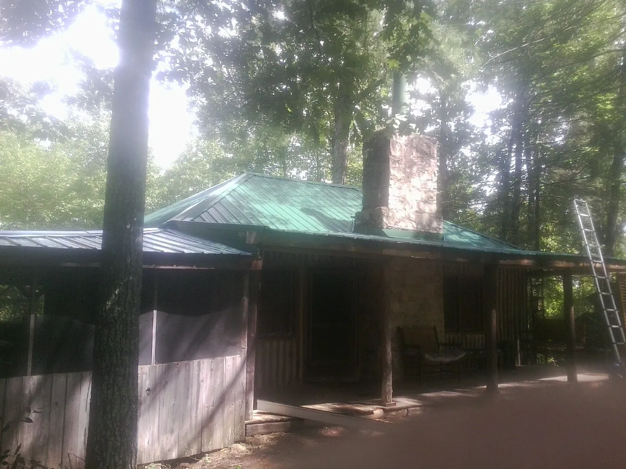 Green metal roof and stone chimney above a log cabin porch in Douglas